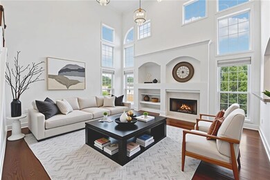 Living room featuring wood finished floors, a warm lit fireplace, built in features, and a towering ceiling