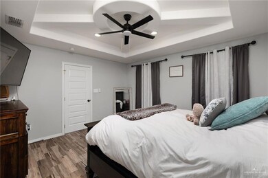 Bedroom with hardwood / wood-style floors, a tray ceiling, and ceiling fan
