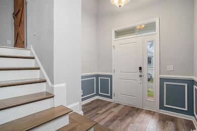 Entryway featuring wood finished floors, stairs, wainscoting, and a decorative wall