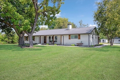 Ranch-style house featuring brick siding, a metal roof, a front lawn, a chimney, and a porch