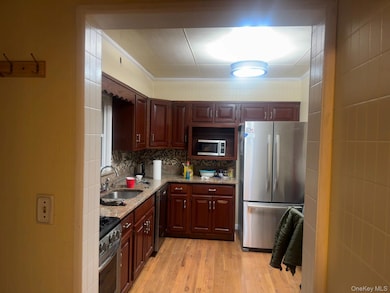 Kitchen with appliances with stainless steel finishes, light wood finished floors, tasteful backsplash, light stone countertops, and ornamental molding