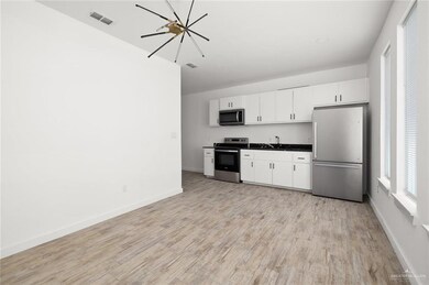 Kitchen featuring stainless steel appliances, dark countertops, a chandelier, white cabinets, and light wood-style flooring