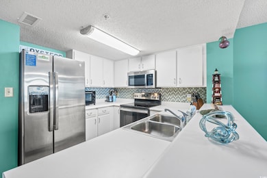 Kitchen featuring sink, white cabinetry, tasteful backsplash, a textured ceiling, and stainless steel appliances