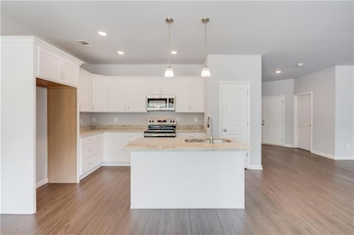 Kitchen with appliances with stainless steel finishes, a sink, light wood-type flooring, light stone countertops, and recessed lighting