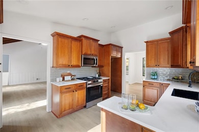 Kitchen featuring brown cabinets, stainless steel appliances, light wood finished floors, backsplash, and recessed lighting