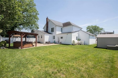 Back of house featuring a hot tub, a patio, a gazebo, a chimney, and a storage shed