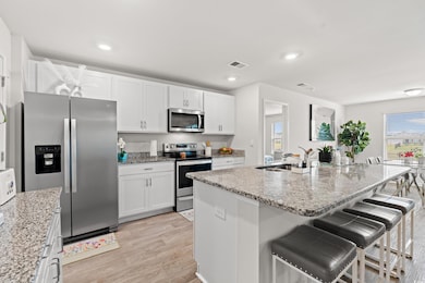 Kitchen featuring appliances with stainless steel finishes, a sink, light wood-type flooring, a kitchen breakfast bar, and white cabinetry