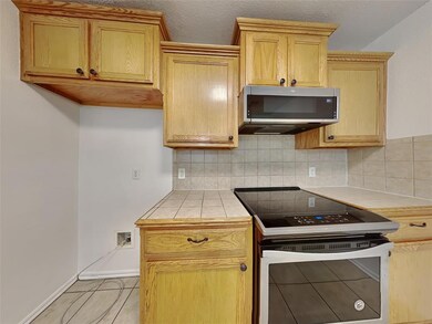 Kitchen with appliances with stainless steel finishes, tile counters, tasteful backsplash, light tile patterned floors, and baseboards