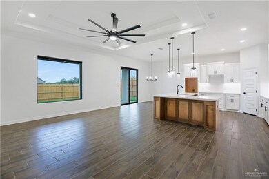 Kitchen featuring a tray ceiling, ceiling fan with notable chandelier, open floor plan, and dark wood-type flooring