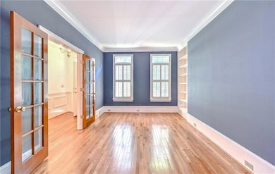 Empty room featuring light wood-style floors, french doors, and crown molding