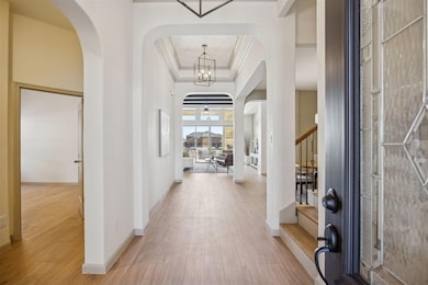 Entrance foyer with stairs, arched walkways, a raised ceiling, light wood finished floors, and crown molding