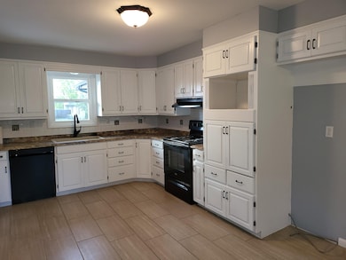 Kitchen featuring black appliances, white cabinetry, decorative backsplash, and under cabinet range hood