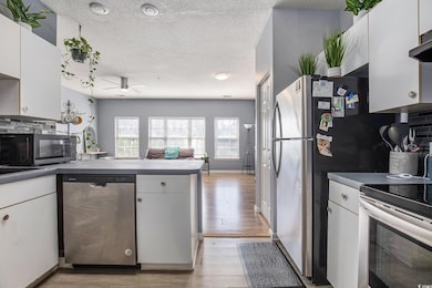 Kitchen with appliances with stainless steel finishes, light wood-style flooring, ceiling fan, a textured ceiling, and decorative backsplash