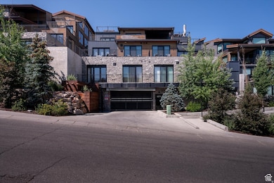 View of front facade with stone siding, concrete driveway, an attached garage, and a balcony
