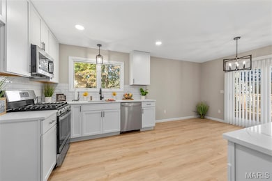 Kitchen with stainless steel appliances, white cabinetry, recessed lighting, backsplash, and light wood-style floors