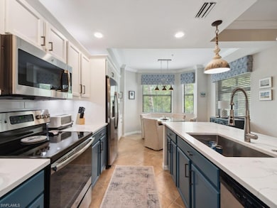 Kitchen featuring stainless steel appliances, blue cabinets, light stone counters, hanging light fixtures, and white cabinets