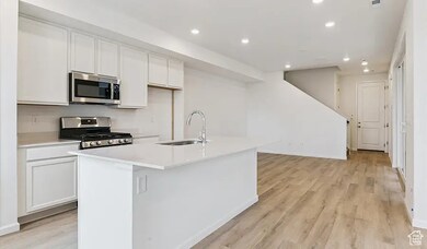Kitchen with recessed lighting, stainless steel appliances, white cabinets, a kitchen island with sink, and light wood-style floors