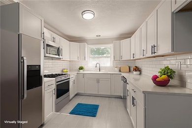Kitchen featuring stainless steel appliances, white cabinetry, backsplash, crown molding, and light stone countertops