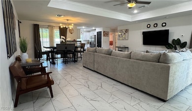 Living room with light marble finish flooring, a chandelier, ornamental molding, a raised ceiling, and a ceiling fan
