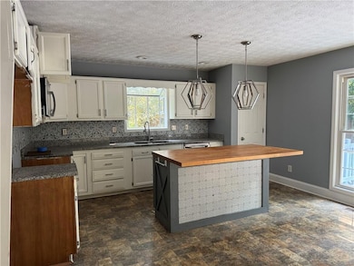 Kitchen featuring wooden counters, stone finish flooring, hanging light fixtures, tasteful backsplash, and a center island