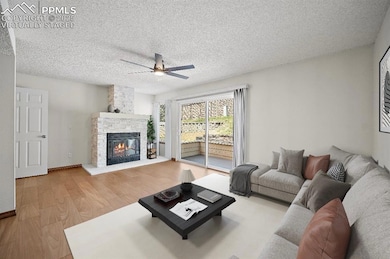 Living area featuring light wood-style flooring, a fireplace, a textured ceiling, and a ceiling fan. This is a virtually staged photo.