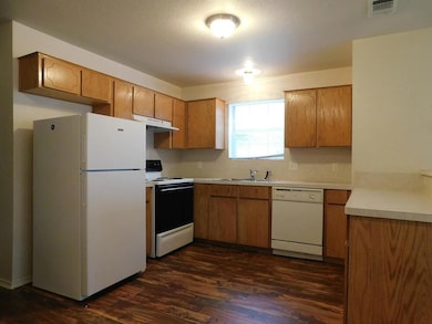 Kitchen featuring white appliances, light countertops, dark wood finished floors, and brown cabinetry
