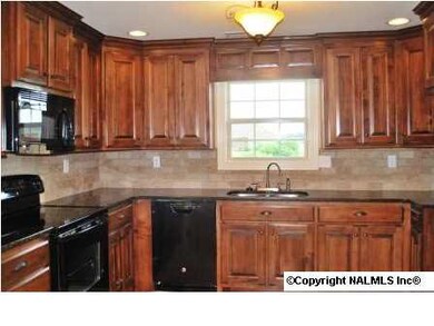 Custom cabinetry with black appliances, tile back splash, granite counter tops and tile flooring.