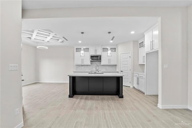 Kitchen featuring white cabinets, backsplash, an island with sink, and light hardwood / wood-style flooring