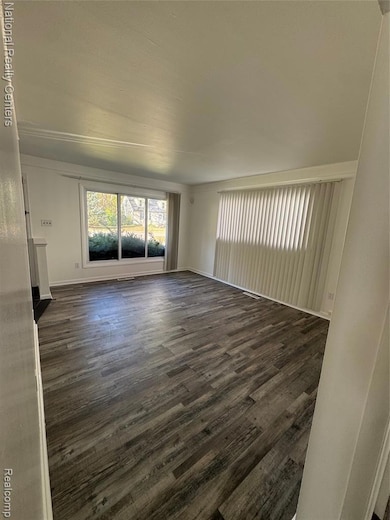 Unfurnished living room with dark wood-type flooring and baseboards
