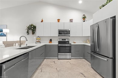 Kitchen featuring quartz countertops, stainless steel appliances, modern gray base cabinets and modern white upper cabinets, and high vaulted ceiling