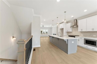 Kitchen with wall chimney range hood, stainless steel microwave, an island with sink, tasteful backsplash, and white cabinetry