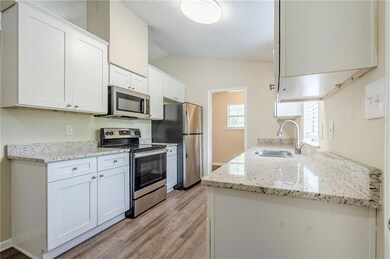 Kitchen featuring stainless steel appliances, a sink, light wood finished floors, lofted ceiling, and white cabinetry