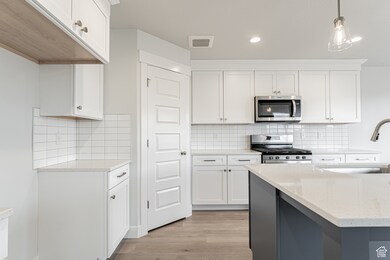 Kitchen featuring visible vents, stainless steel appliances, white cabinetry, a sink, and light wood-style floors