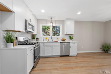 Kitchen with white cabinets, stainless steel appliances, recessed lighting, light wood finished floors, and decorative backsplash