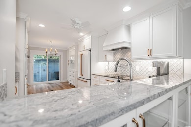 Kitchen with crown molding, backsplash, white cabinetry, light stone counters, and high end white fridge