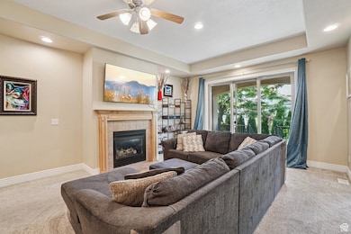 Living area featuring light colored carpet, a tray ceiling, a tiled fireplace, and recessed lighting