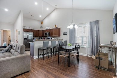 Dining area with high vaulted ceiling, a chandelier, dark wood-style floors, and baseboards