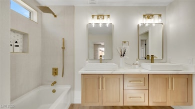 Full bathroom featuring double vanity, washtub / shower combination, and light wood-style flooring