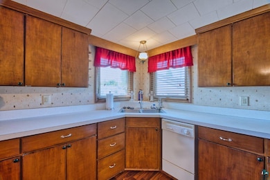 Kitchen featuring dishwasher, light countertops, brown cabinets, and dark wood-style floors