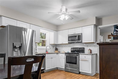 Kitchen with white cabinetry, appliances with stai