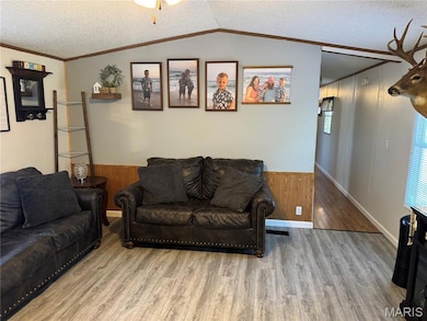 Living room with a textured ceiling, wood finished floors, wooden walls, and crown molding
