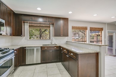 Kitchen with light stone counters, recessed lighting, appliances with stainless steel finishes, dark brown cabinetry, and a peninsula