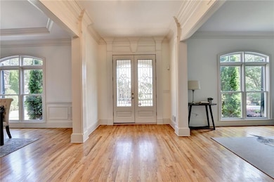 Foyer entrance featuring healthy amount of natural light, light wood-style flooring, french doors, crown molding, and a decorative wall