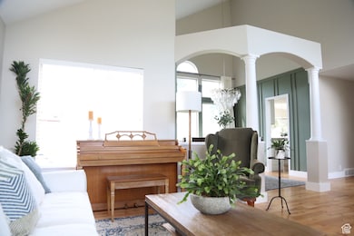 Living area with decorative columns, vaulted ceiling, arched walkways, wood finished floors, and baseboards