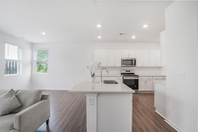 Kitchen featuring stainless steel appliances, a sink, open floor plan, white cabinetry, and tasteful backsplash