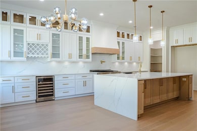 Kitchen with decorative backsplash, decorative light fixtures, light stone counters, white cabinetry, and beverage cooler