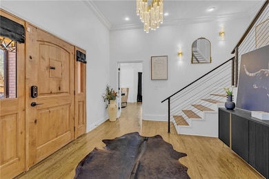 Foyer with ornamental molding, stairs, a chandelier, light wood-style flooring, and recessed lighting