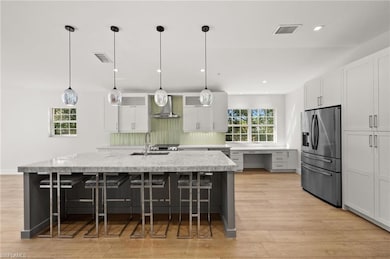 Kitchen featuring stainless steel refrigerator with ice dispenser, wall chimney exhaust hood, a kitchen bar, white cabinetry, and light wood-type flooring