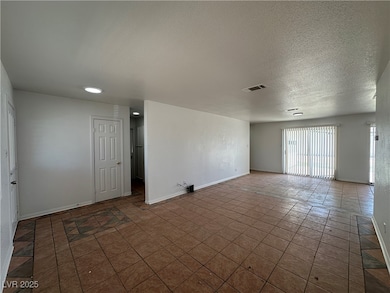 Tiled empty room with a textured ceiling and baseboards