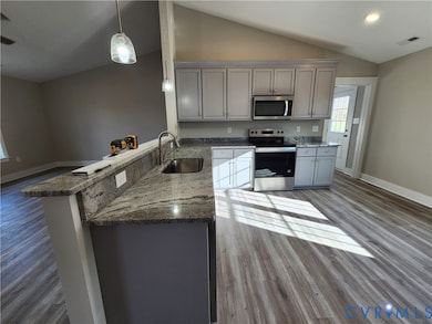 Kitchen with light stone counters, gray cabinetry, appliances with stainless steel finishes, light wood finished floors, and vaulted ceiling
